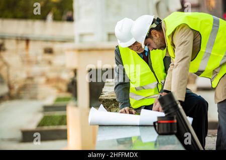 Deux ouvriers du bâtiment examinent les plans sur le papier tout en ayant une conversation importante, gros plan Banque D'Images