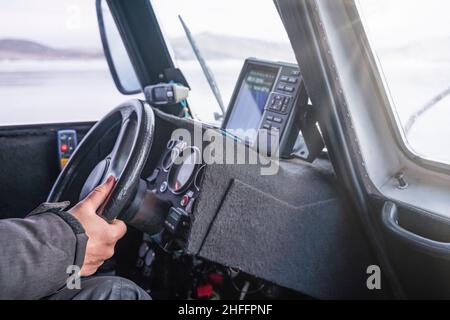 Main rapprochée du conducteur tenant le volant tout en conduisant un aéroglisseur qui se déplace sur le lac gelé Baikal, concept de mode de vie de voyage. Banque D'Images