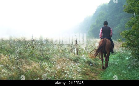 Tôt le matin dans une prairie en fleurs.Homme âgé à cheval.Un homme qui aime l'équitation rencontre l'aube Banque D'Images