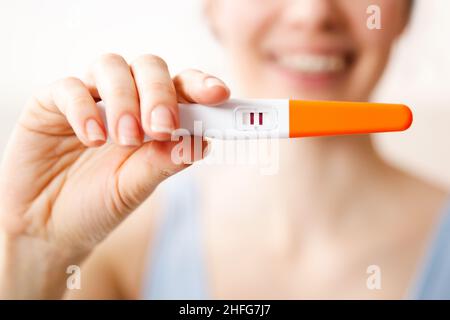 Une jeune femme heureuse tient un test de grossesse positif dans sa main, le concept d'une grossesse longtemps attendue. Banque D'Images