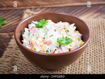 Salade avec des bâtonnets de maïs et de crabe dans un bol sur une table en bois.Cuisine russe traditionnelle. Banque D'Images