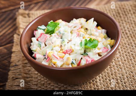 Salade avec des bâtonnets de maïs et de crabe dans un bol sur une table en bois.Cuisine russe traditionnelle. Banque D'Images