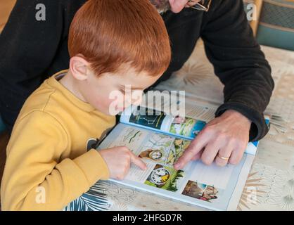 un garçon de 6 ans étudie avec l'aide de son père.L'enfant lit à partir d'un livre et le père lui explique Banque D'Images