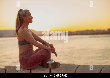 Femme en sportewear méditant en position lotus au bord de la mer Banque D'Images