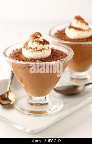 Desserts à la mousse au chocolat dans des plats coniques en verre sur un plateau de service en porcelaine blanche avec des cuillères, recouvert de tourbillons de crème et de chocolat noir râpé Banque D'Images