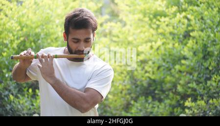 Un musicien indien de sexe masculin jouant à Bansuri portant un t-shirt blanc .Prise de vue en extérieur sur fond vert Banque D'Images