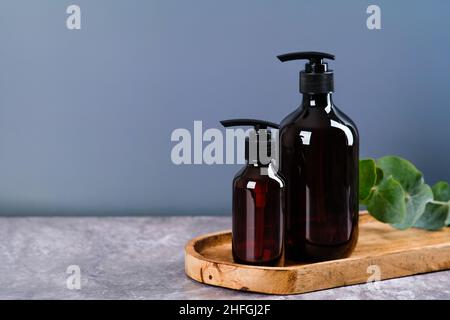 Flacons de distribution en verre ambré avec gel douche et shampooing, feuilles d'eucalyptus sur panneau en bois.ENSEMBLE de produits de beauté naturels SPA.Emballages cosmétiques des Banque D'Images
