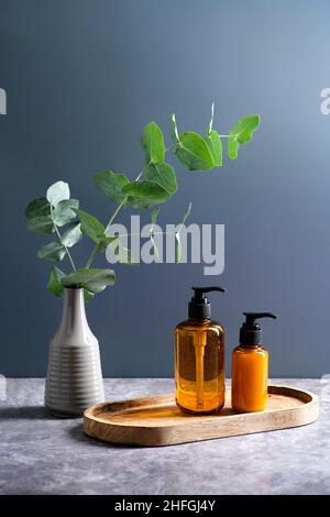 Flacons de distribution en verre ambré et vase avec plante d'eucalyptus sur fond bleu foncé.Ensemble de cosmétiques naturels biologiques POUR LE SPA.Récipients avec shampooing et s Banque D'Images