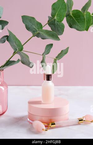 Récipients de cosmétiques roses et rouleau de massage du visage sur la table à l'eucalyptus.Concept de soin du visage.Design d'emballage des produits de beauté Banque D'Images