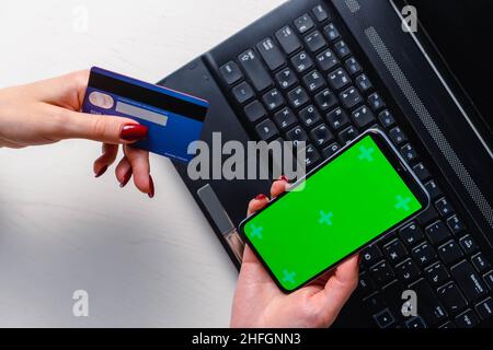 Gros plan des mains de femme utilisant un smartphone écran vert vierge maquette et tenant la carte de crédit Banque D'Images