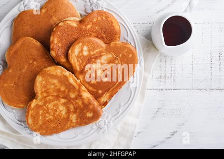 Crêpes avec confiture de baies et miel en forme de coeur et une tasse de café chaud sur fond de bois blanc.Petit déjeuner concept pour la Saint Valentin ou le plaisir Banque D'Images