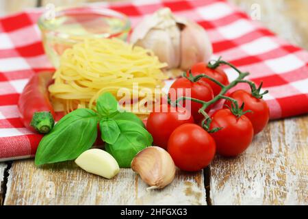 Ingrédients pour la cuisson des pâtes : tagliatelle, tomates cerises, ail, basilic frais, piment et bol d'huile d'olive sur toile à carreaux Banque D'Images