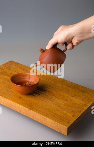 La main d'un homme verse du thé pu erh fraîchement préparé d'une théière en argile dans une tasse traditionnelle.Une tasse sur une table pour les cérémonies du thé. Banque D'Images