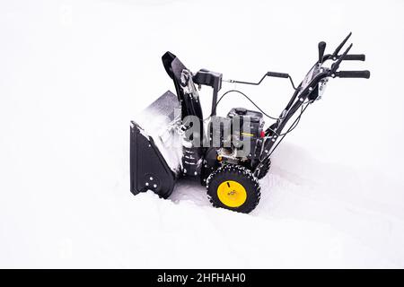 Mini chasse-neige noir avec roue jaune sur fond de neige blanche.Déneigement en hiver à l'arrière-cour.La technologie pour aider les gens. Banque D'Images