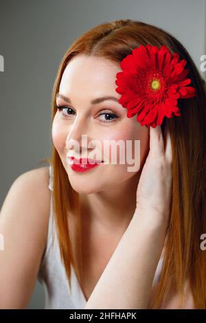 Portrait d'une femme adulte 40 avec fleur rouge et rouge à lèvres. Banque D'Images