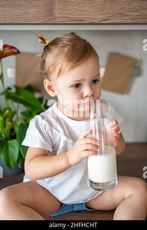 Bonne petite fille assise à la table dans la cuisine et buvant du lait Banque D'Images