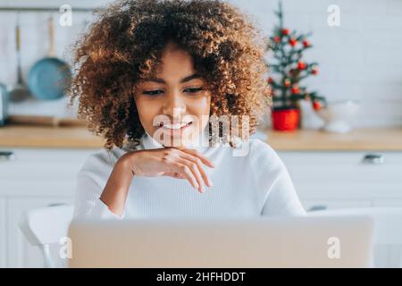 Jeune acheteur à la peau sombre et excitée avec des cheveux tendance dans les sourires d'ordinateur portable et aime faire du shopping en ligne à proximité Banque D'Images