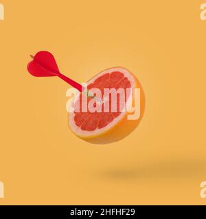 Tranche de pamplemousse, fruit avec cible circulaire marquée et dart rouge sur fond orange.Idée minimale de nourriture et de fruits concept.idée créative à produire Banque D'Images