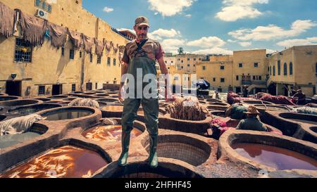 Fès, Maroc - avril 2018 : Tanner travaillant dans les pots de teinture de Chouara Tannery peignant des cuirs d'animaux.Puits ronds en pierre remplis de colorant ou de blanc Twin Banque D'Images