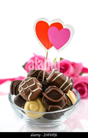 Pralines au chocolat dans un bol en verre et bouquet de roses roses sur fond blanc.Concept de la Saint-Valentin et de la fête des femmes, mise au point sélective. Banque D'Images