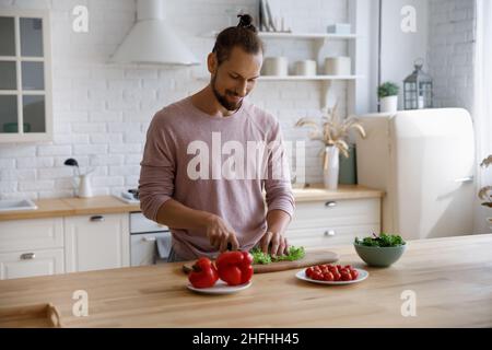 Joyeux jeune homme beau préparant des aliments sains dans la cuisine. Banque D'Images
