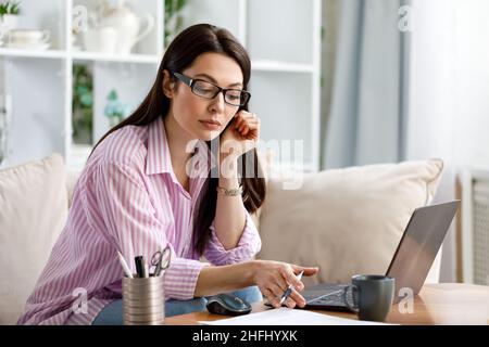 Portrait d'une femme brune travaillant à la maison sur un ordinateur portable. Banque D'Images