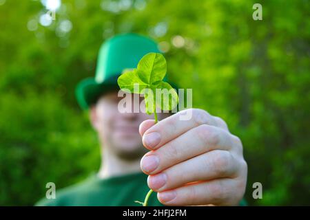 Saint Patrick Background.Homme en chapeau de lepreun vert avec des fleurs de trèfle et le drapeau de l'Irlande dans ses mains dans un jardin de printemps.Irish Traditional Banque D'Images