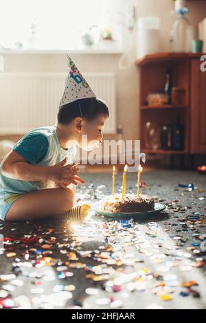 Garçon célébrant son anniversaire bougies soufflantes sur un gâteau fait maison assis sur le sol.Fête d'anniversaire.Mets sucrés. Banque D'Images