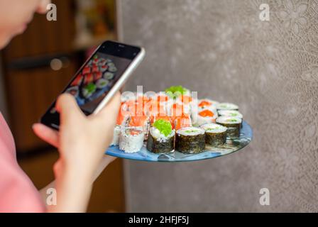 Faire des sushis et des petits pains à la maison.Sushi avec fruits de mer, salade et riz blanc.Nourriture pour la famille et les amis.Une fille prend des photos sur son téléphone d'un ensemble de Banque D'Images