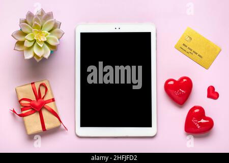 Tablette numérique pour choisir des cadeaux, faire l'achat, enveloppe, coeur rouge sur table rose vue du dessus plat Lay liste d'achats de vacances, bonne Saint-Valentin Banque D'Images
