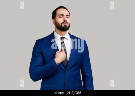 Portrait de l'homme barbu se pointant vers lui-même et regardant égoïste haughty égoïste, se sentant fier de sa propre réalisation, portant le costume de style officiel.Prise de vue en studio isolée sur fond gris. Banque D'Images