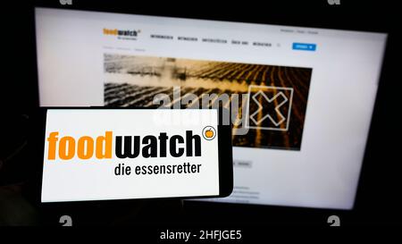 Personne tenant un téléphone portable avec le logo du groupe de plaidoyer allemand Foodwatch e.V. sur l'écran devant le site de l'association.Mise au point sur l'affichage du téléphone. Banque D'Images