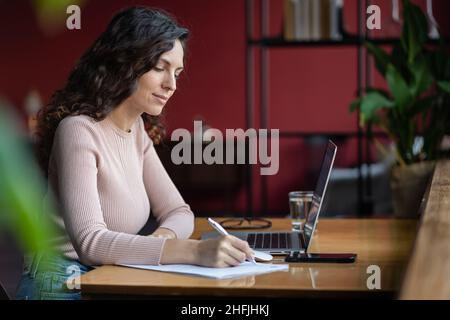 Étude ciblée de fille sur ordinateur portable prendre des notes.Propriétaire concentré de petites entreprises avec écriture pc dans ordinateur portable Banque D'Images