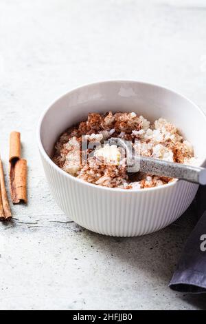 Porridge de riz scandinave à la cannelle et au beurre dans un bol blanc sur fond gris.Concept de cuisine norvégienne. Banque D'Images