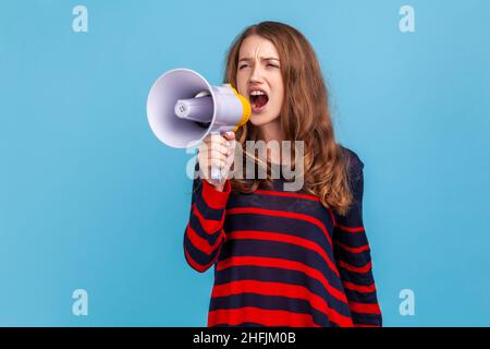 Portrait d'une femme portant un chandail rayé de style décontracté, criant bruyamment en mégaphone, annonçant une importante publicité, protestant.Studio d'intérieur isolé sur fond bleu. Banque D'Images