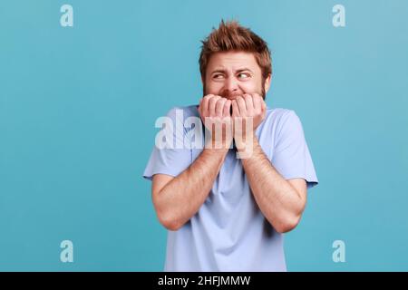 Trouble anxieux.Portrait de l'homme stressé, inquiet barbu piquant les ongles, nerveux au sujet des troubles, paniquant et regardant peur.Studio d'intérieur isolé sur fond bleu. Banque D'Images