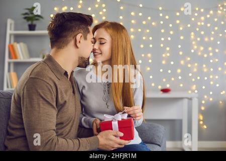 Un jeune couple affectueux s'embrasse pendant les cadeaux et les fêtes à la maison Banque D'Images