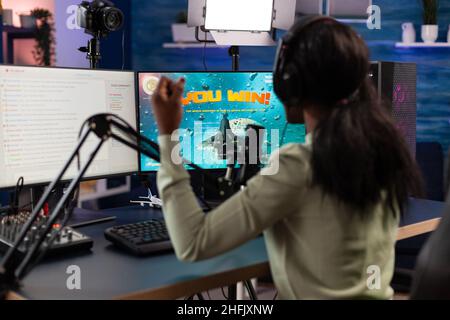 Excitée heureuse esport femme jouant en ligne jeux vidéo gagnant l'espace de tir tournoi.Un joueur qui a réussi à parler avec des lecteurs à distance lors de discussions en streaming à l'aide du clavier RVB dans un studio à domicile Banque D'Images
