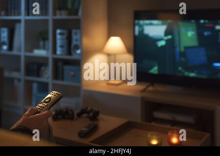 Homme se reposant sur le canapé à la maison et regardant la télévision, il tient la télécommande Banque D'Images