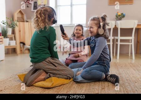 Petites filles avec casque et microphone prenant un entretien, s'amuser et jouer à la maison. Banque D'Images