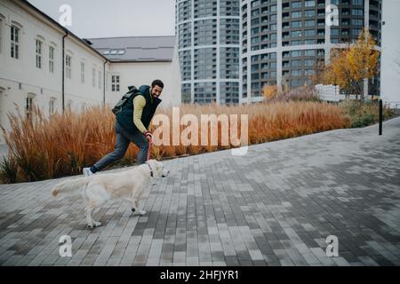 Un jeune homme heureux qui court avec son chien en laisse à l'extérieur de la ville. Banque D'Images