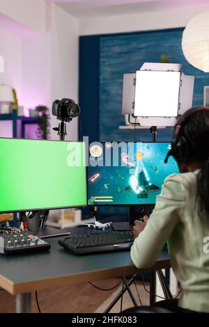 Gamer femme jouant des jeux vidéo en ligne pendant le championnat de jeu de pillage à mok up écran vert chroma ordinateur clé avec affichage isolé.Jeu de tir en streaming pour jeunes joueurs utilisant le joystick Banque D'Images