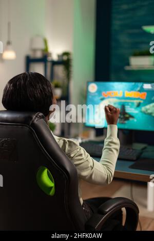 Bonne joueuse professionnelle excitée, femme assise à un bureau dans un studio de jeu à la maison, jouant à l'espace de tir jeux vidéo gagnant le championnat en ligne.Joueur gagnant utilisant un équipement informatique RVB.Jeu d'espace cybernétique Banque D'Images