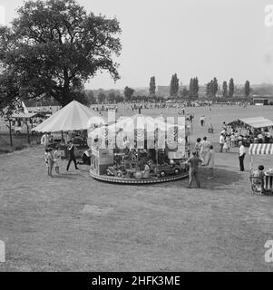 Laing Sports Ground, Rowley Lane, Elstree, Barnett, Londres,14/06/1969.Vue sur un manège et des stands du parc des expositions, où la foule se rassemblait sur un terrain de sport au-delà, lors d'une journée de gala qui se tiendra au stade de Laing à Elstree.Le 14th juin 1969, Laing a tenu une journée de gala au stade de Laing, en remplacement de la Journée annuelle des sports.Le club sportif a organisé des manifestations sportives, notamment des tournois de hockey, de tennis, de pétanque et de football.Un programme anglais traditionnel de la tête comprenait des noix de coco, du bingo, des promenades en poney, un service de traiteur et une tente à bière, des bonbons en soie dentaire et des ronds-points.La journée s'est terminée Banque D'Images