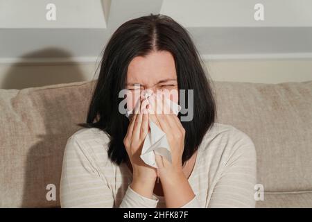 Femme adulte d'âge moyen souffrant de rhinite allergique à la maison.Symptômes de rhume ou d'allergie.La femme éternue dans un mouchoir blanc. Banque D'Images