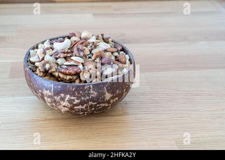 Les noix se mélangent dans un bol en bois de noix de coco sur fond de bois Banque D'Images