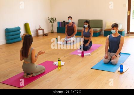 Femme instructeur avec des hommes et des femmes multiraciaux portant des masques dans le studio de yoga pendant le Covid-19 Banque D'Images