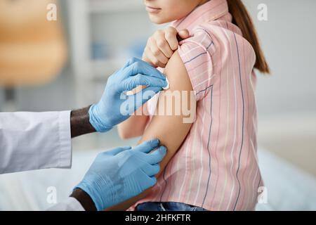 Gros plan de la petite fille mignonne se faire vacciner avec un médecin essuyant l'épaule à la clinique de vaccination des enfants Banque D'Images