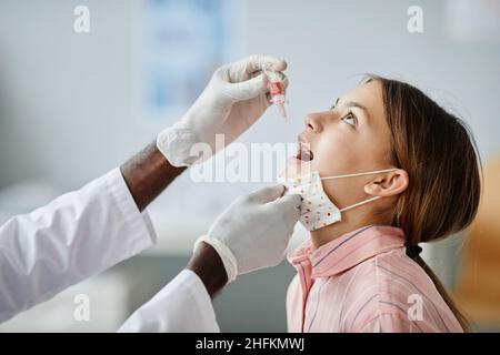 Vue latérale du médecin qui goutte du liquide dans la bouche de l'enfant pendant la vaccination orale en clinique Banque D'Images