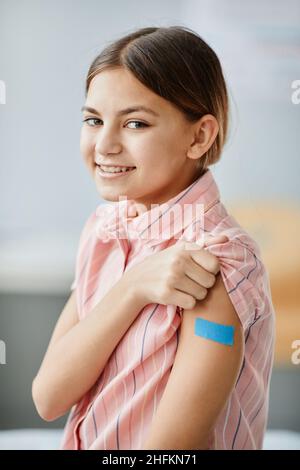 Portrait vertical de petite fille souriante montrant l'épaule avec le plâtre après avoir été vaccinée contre le covid 19 Banque D'Images